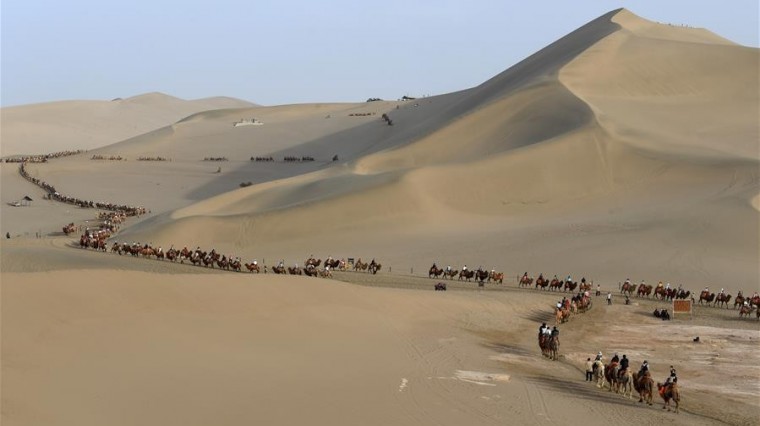 Des visiteurs à dos de chameau dans le site touristique de la Source du Croissant de lune et des dunes Mingsha